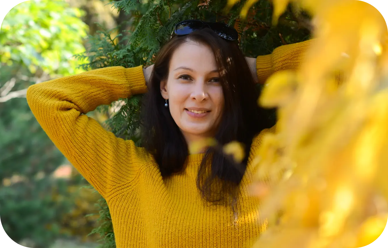 Світлана Отенко стоїть біля дерев із жовтим і зеленим листям